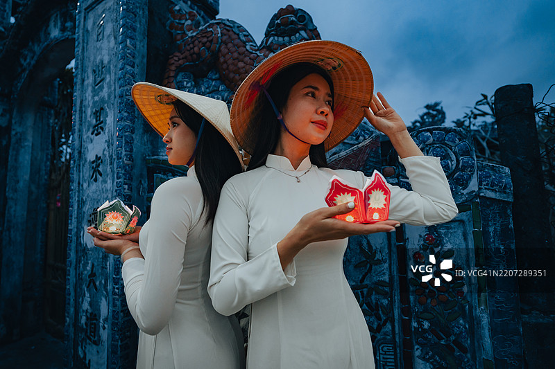 越南女孩手持花环和彩色灯笼，身穿奥黛，站在越南顺化市。图片素材