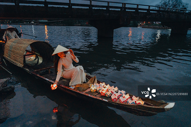 传统的多彩纸灯笼在夜晚漂浮在河上，旁边是一位身着越南传统服饰的美丽女性。图片素材