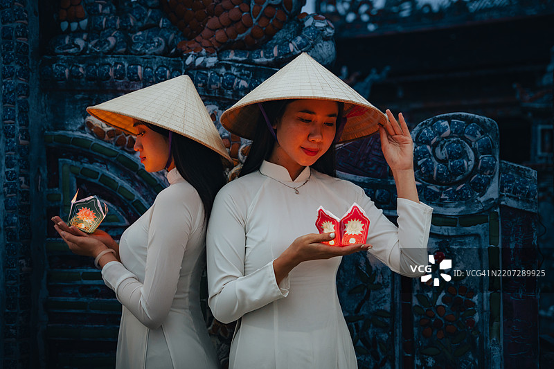 越南女孩手持花环和彩色灯笼，身穿奥黛，站在越南顺化市。图片素材