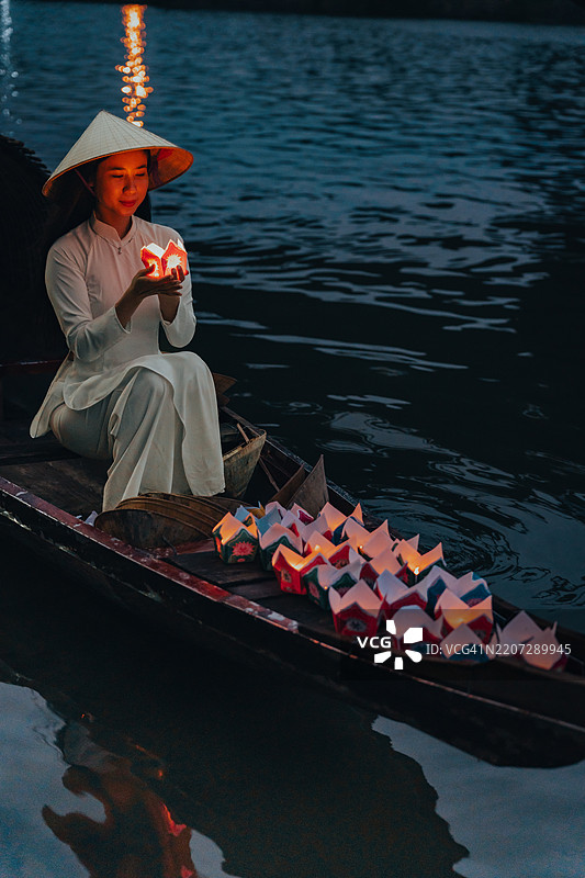 传统的多彩纸灯笼在夜晚漂浮在河上，旁边是一位身着越南传统服饰的美丽女性。图片素材