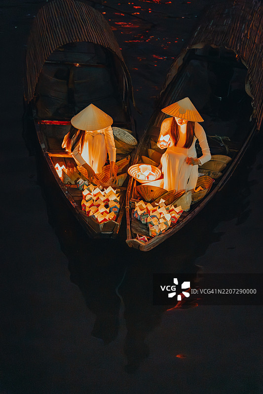 传统的多彩纸灯笼在夜晚漂浮在河上，旁边是一位身着越南传统服饰的美丽女性。图片素材