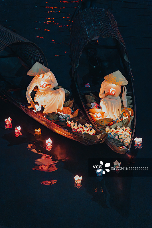 传统的多彩纸灯笼在夜晚漂浮在河上，旁边是一位身着越南传统服饰的美丽女性。图片素材