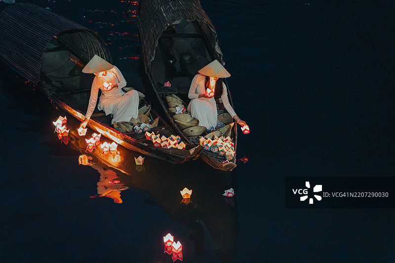 传统的多彩纸灯笼在夜晚漂浮在河上，旁边是一位身着越南传统服饰的美丽女性。图片素材