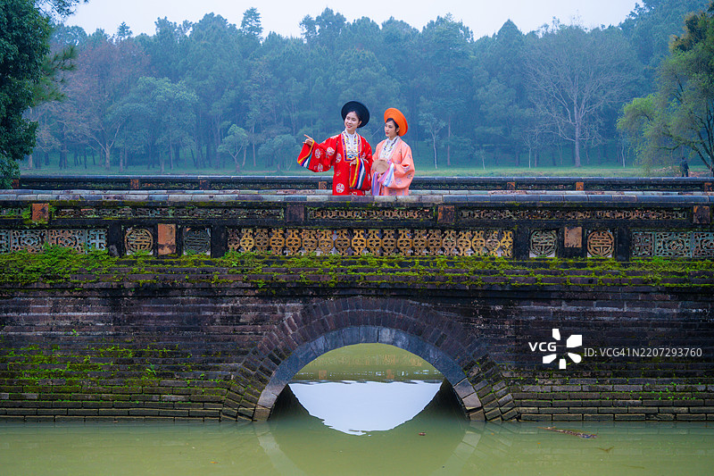 两位年轻的越南女性穿着名为“日平”的新年庆祝服装，站在越南顺化的明命皇陵前。图片素材