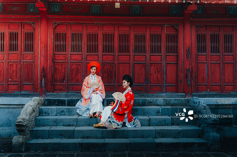 两位年轻的越南女性穿着名为“日平”的新年庆祝服装，站在越南顺化的明命皇陵前。图片素材