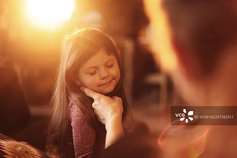 美丽的小女孩微笑着，母亲坐在沙发上轻抚她，夕阳下的温馨时刻。图片素材