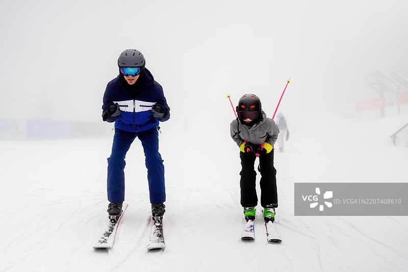 男人和孩子在雪山坡上并肩滑雪图片素材