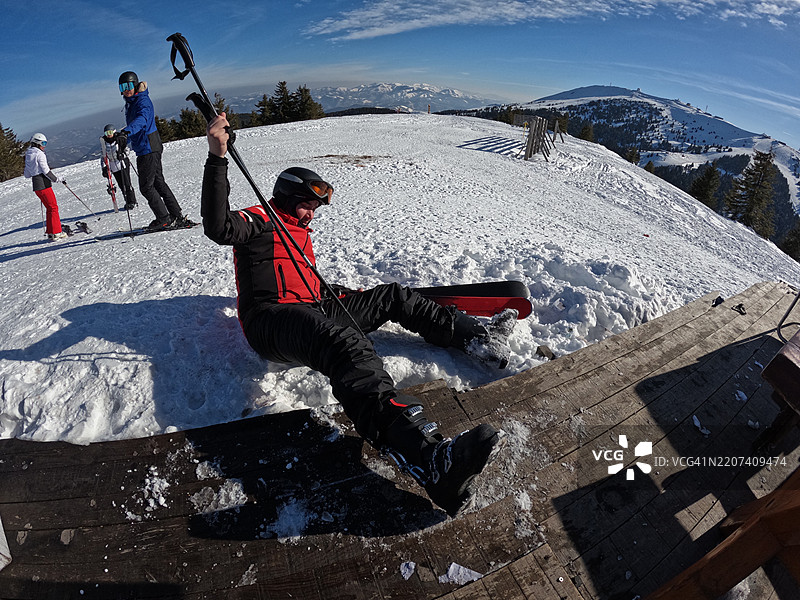 男子在风景如画的山区滑雪坡上摔倒，手中握着滑雪杖图片素材