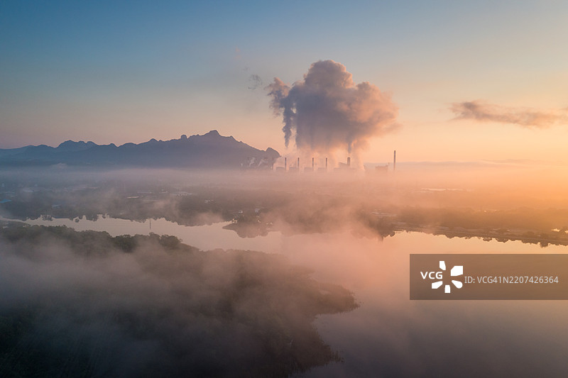 空中俯瞰早晨的煤电厂，旁边有一个池塘，水面上倒映着高耸烟囱冒出的白色蒸汽。煤电厂。图片素材