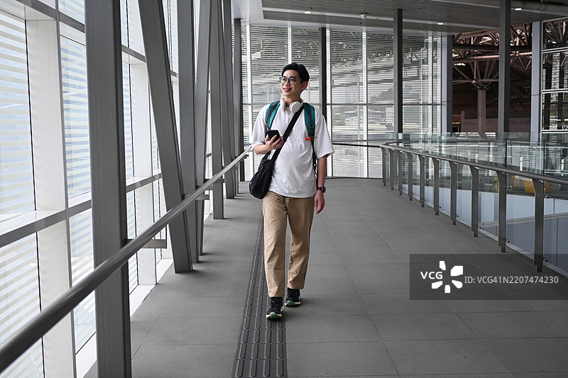 这个男人背着背包，面带微笑，正朝火车站走去。图片素材