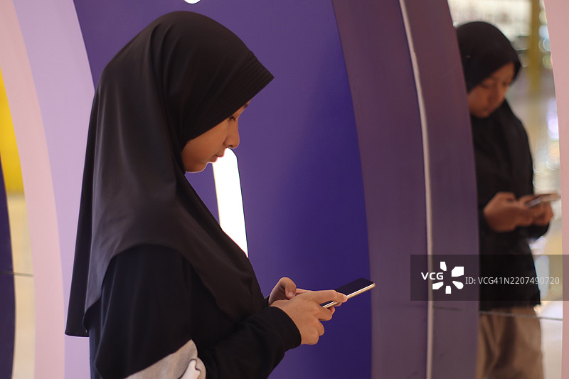 一个女孩在镜子前使用智能手机。图片素材