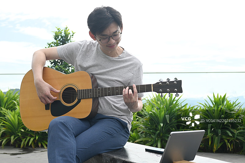 年轻男子坐在屋顶上弹奏木吉他图片素材