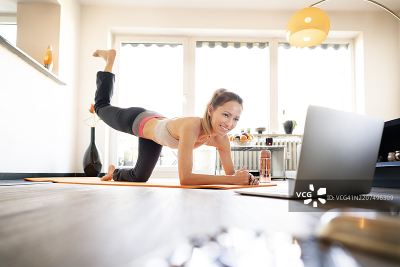 成熟的女性在家中跟随在线教程练习瑜伽图片素材