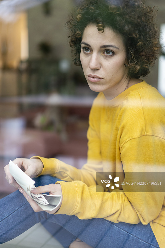 严肃的女人坐在家里的窗边，手里拿着照片。图片素材