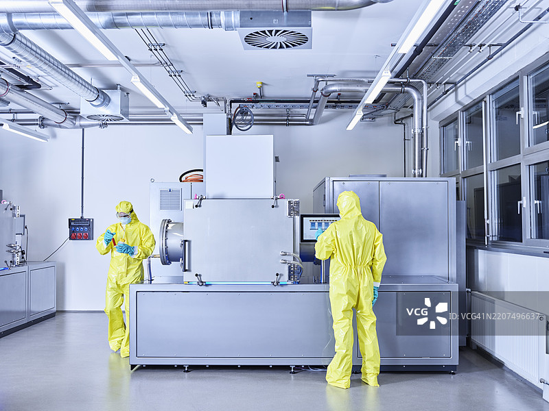 化学家在工业实验室工作，穿着防护服在洁净室内。图片素材