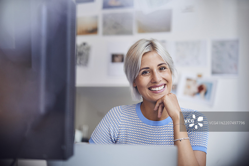 年轻女性在办公室工作，坐在桌子旁，面带微笑图片素材