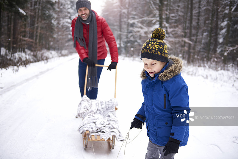 小男孩和他的父亲在冬季森林里玩雪橇图片素材