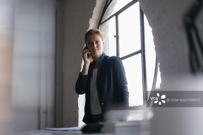 办公室窗边的女商人正在使用手机图片素材