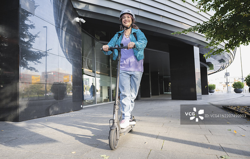 女子在城市的人行道上骑电动滑板车图片素材