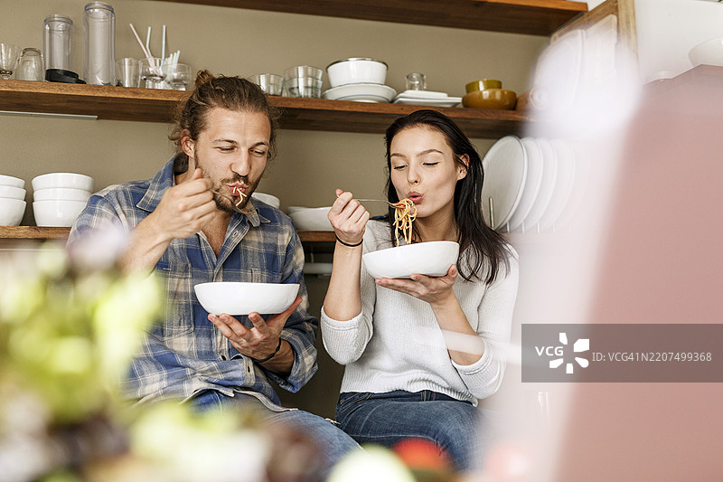 快乐的情侣坐在厨房里，吃意大利面图片素材
