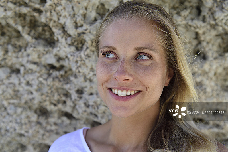 微笑的金发女性肖像，背景为岩石景观图片素材