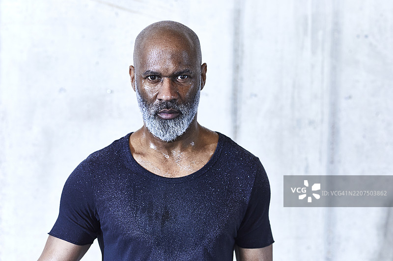 一位满头大汗的光头男子，留着灰色胡须，穿着深蓝色运动衫。图片素材