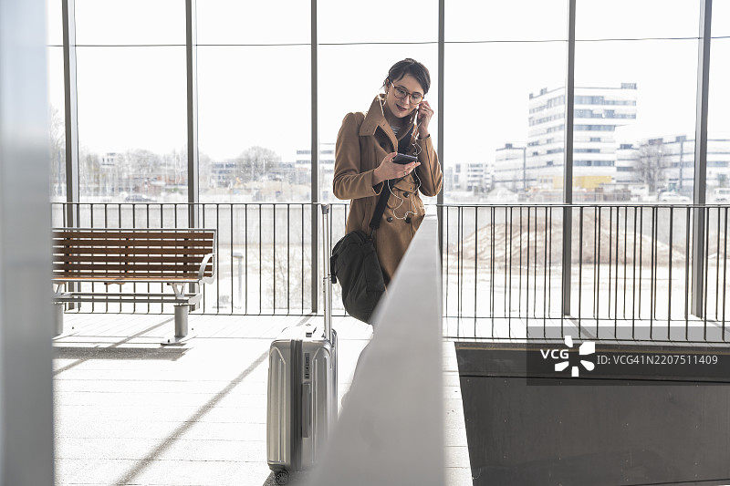 一位带着行李和手机的女商人正在佩戴耳机图片素材