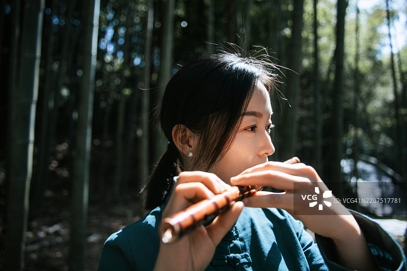 身穿传统服装的亚洲女性在竹林中吹奏笛子图片素材