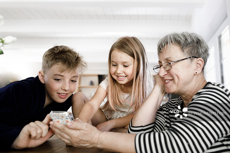 快乐的祖母和孙子孙女在家里使用手机图片素材