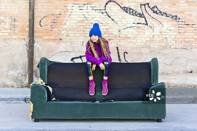 穿着色彩缤纷衣服的女孩坐在户外的沙发上图片素材