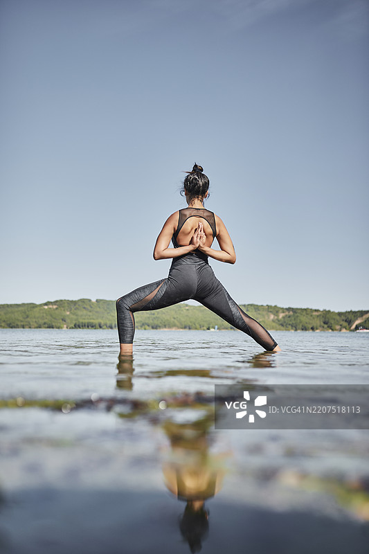 年轻女性在湖边做瑜伽，战士姿势，背影图片素材