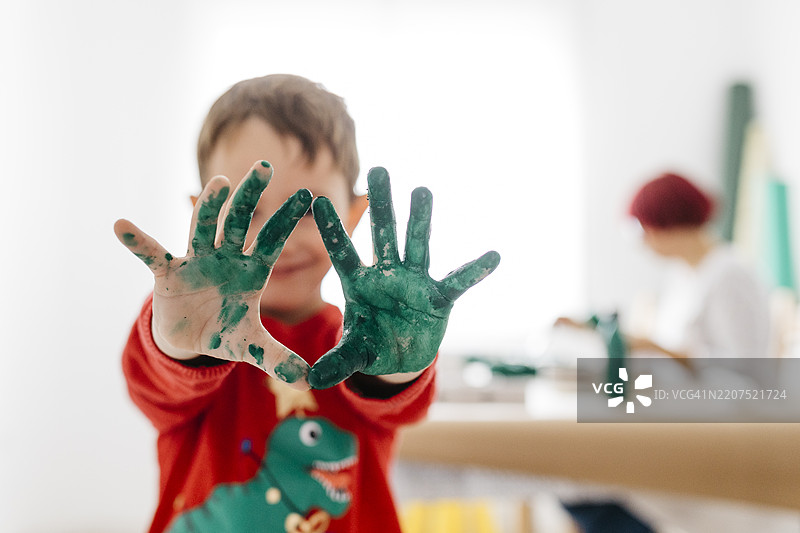 男孩在家做手工艺，手上涂着绿色颜料。图片素材