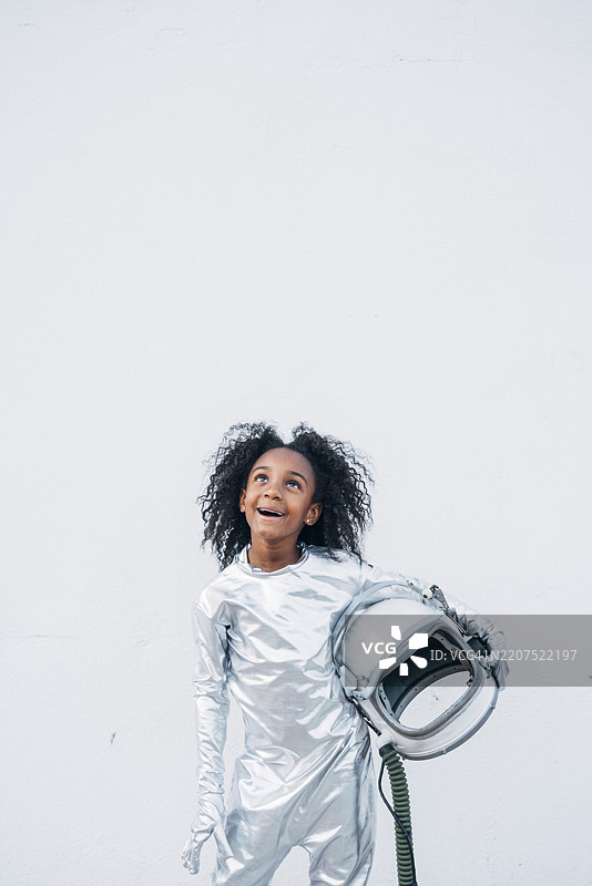 惊讶的小女孩穿着宇航服，站在白色背景前仰望。图片素材