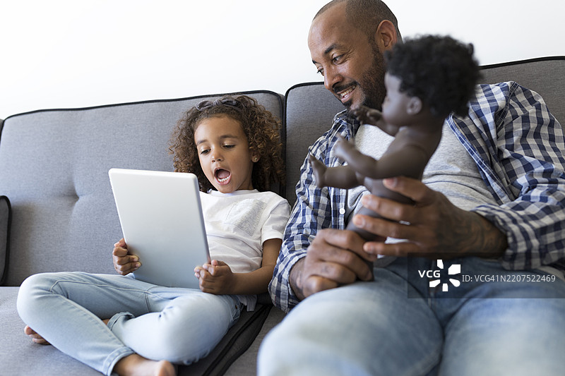 父亲和兴奋的女儿坐在家里的沙发上看平板电脑图片素材