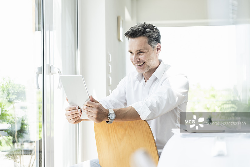 成熟男性坐在椅子上，背对着椅背，使用平板电脑图片素材