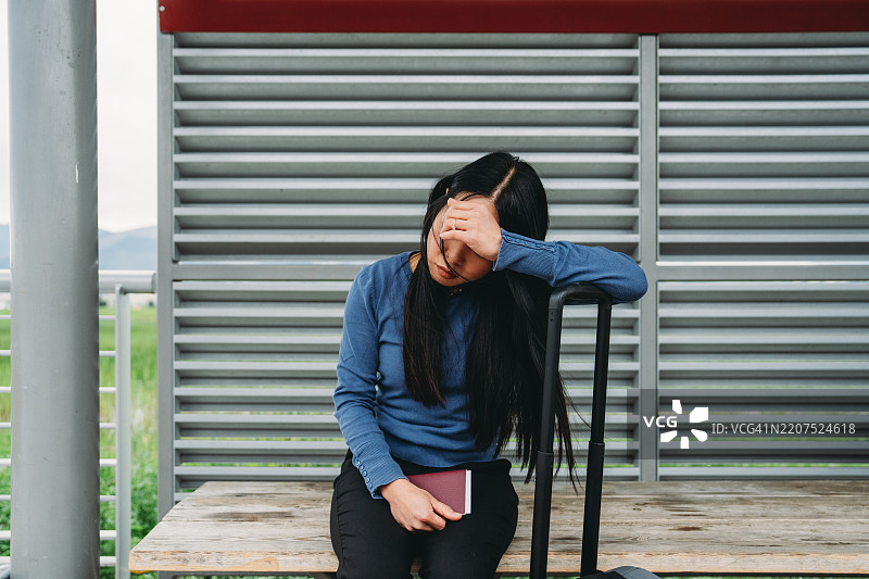 年轻女性在公交车站等候，手里拿着护照和行李图片素材