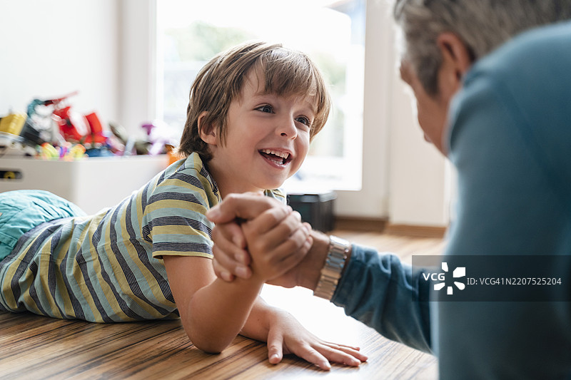 父亲和儿子在家里躺在地板上摔跤。图片素材
