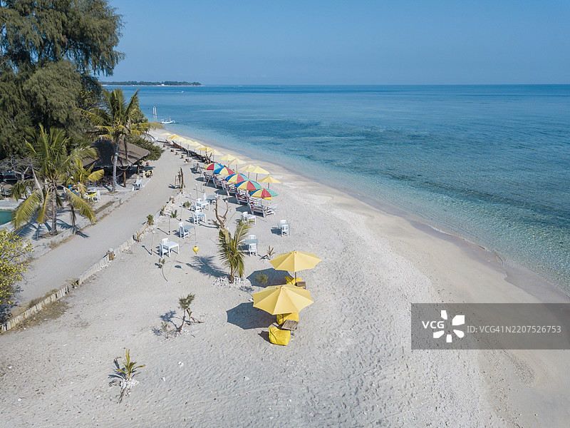 巴厘岛吉利艾尔岛上，椅子和五彩伞在晴朗的蓝天下排列的无人机视角图片素材