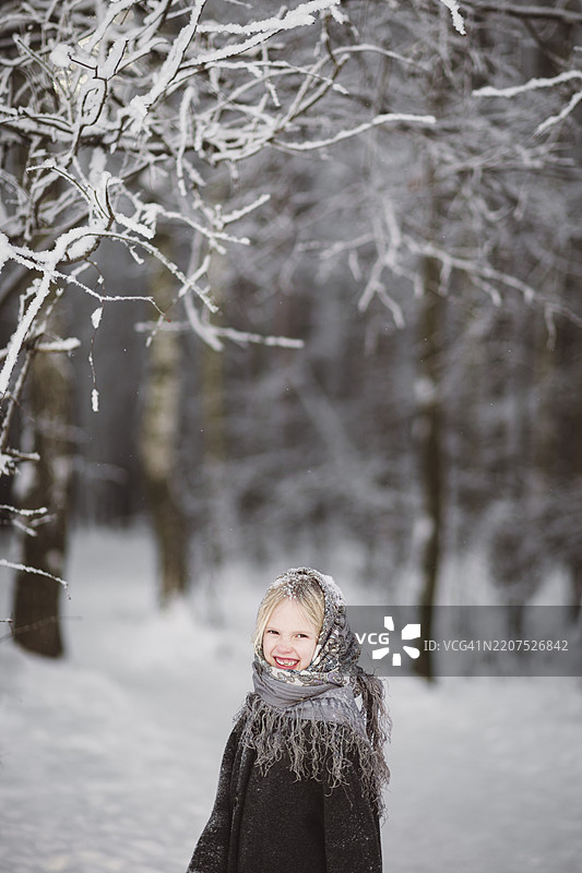快乐的小女孩戴着头巾，站在冬季森林前。图片素材