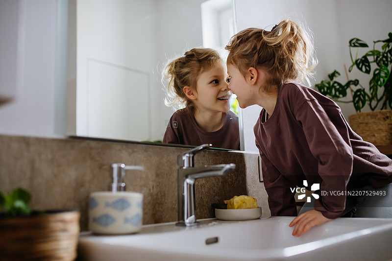 小女孩坐在浴室里，凝视着自己的倒影。图片素材