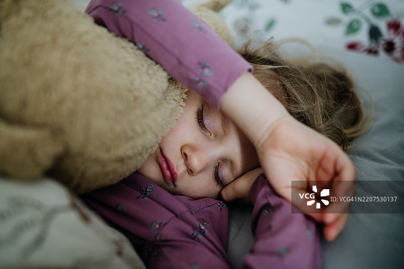 女孩抱着她的泰迪熊玩具睡觉的肖像。图片素材
