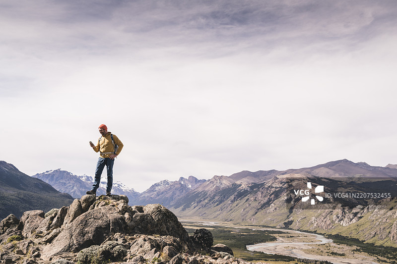 成熟男性在岩石上站立，使用智能手机，背景是天空，阿根廷巴塔哥尼亚。图片素材