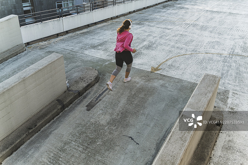 女性运动员在日落时分在阳台上慢跑时戴着耳机听音乐图片素材