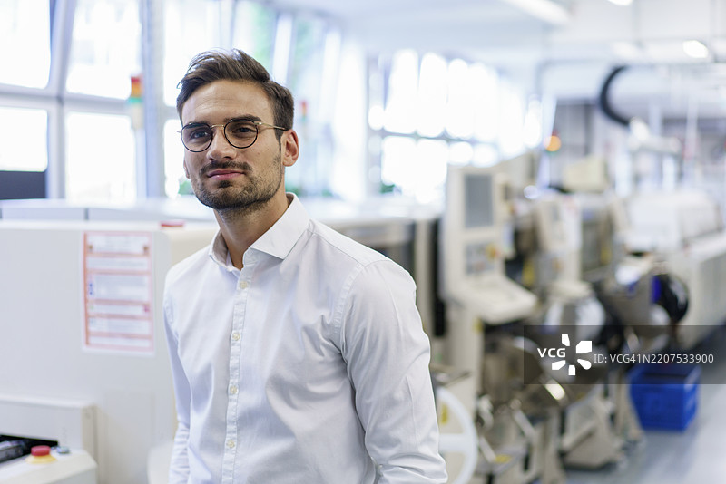 深思的年轻男性专业人士站在灯光照亮的工厂内图片素材