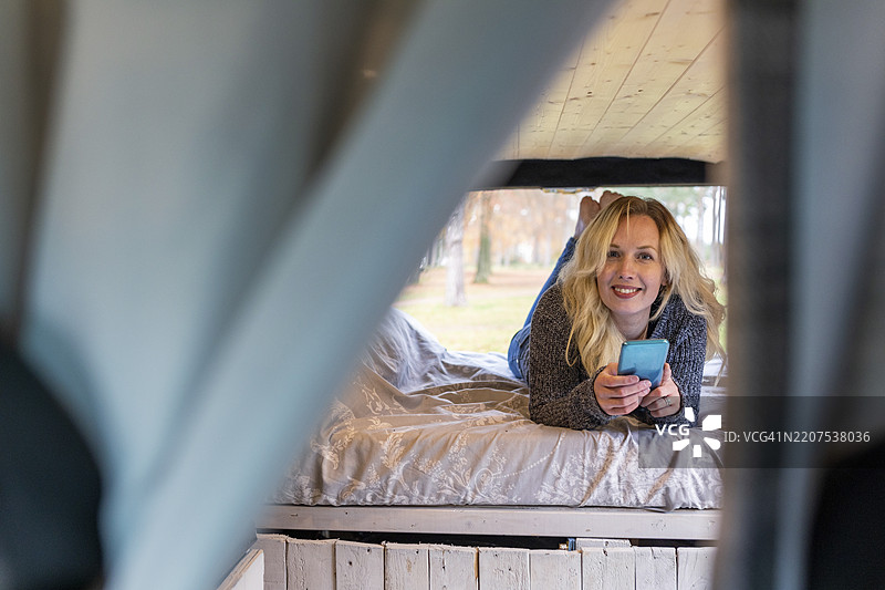 微笑的女性在面包车的床上拿着手机图片素材
