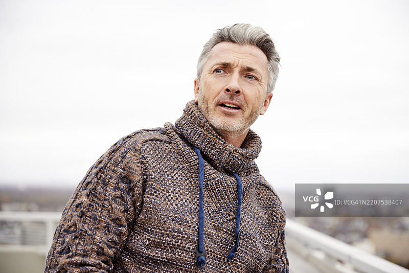 微笑的男人站在天空下，目光投向远方图片素材