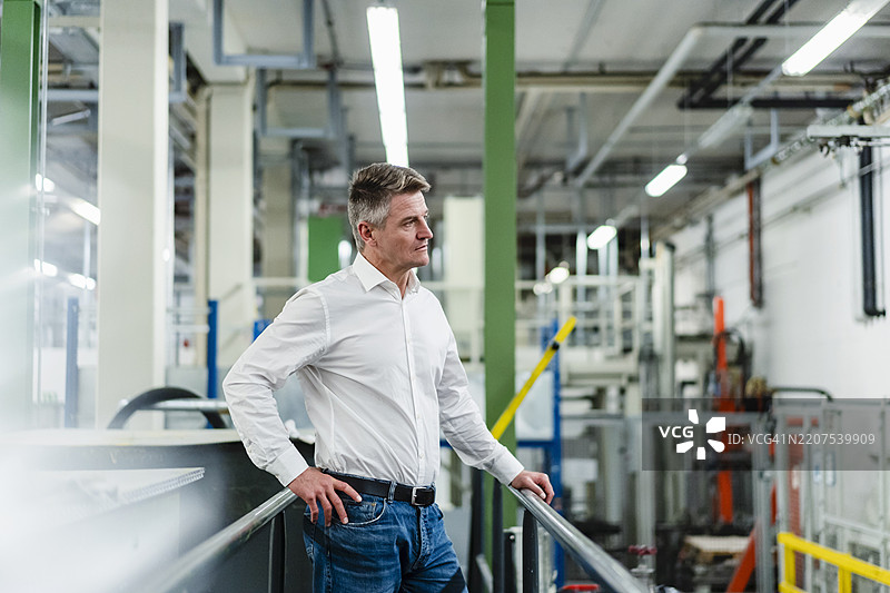 男性专业人士手放在臀部，站在工业环境中沉思。图片素材