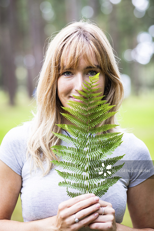 微笑的年轻女性用蕨类植物叶子遮住脸部图片素材