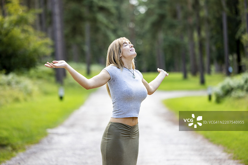 微笑的女性在森林中的道路上双臂高举图片素材
