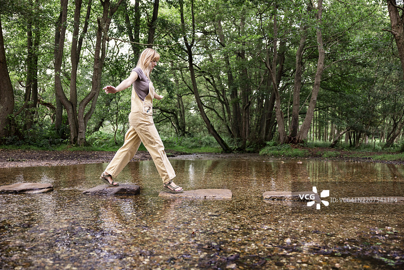 年轻女性在河中走在岩石上图片素材